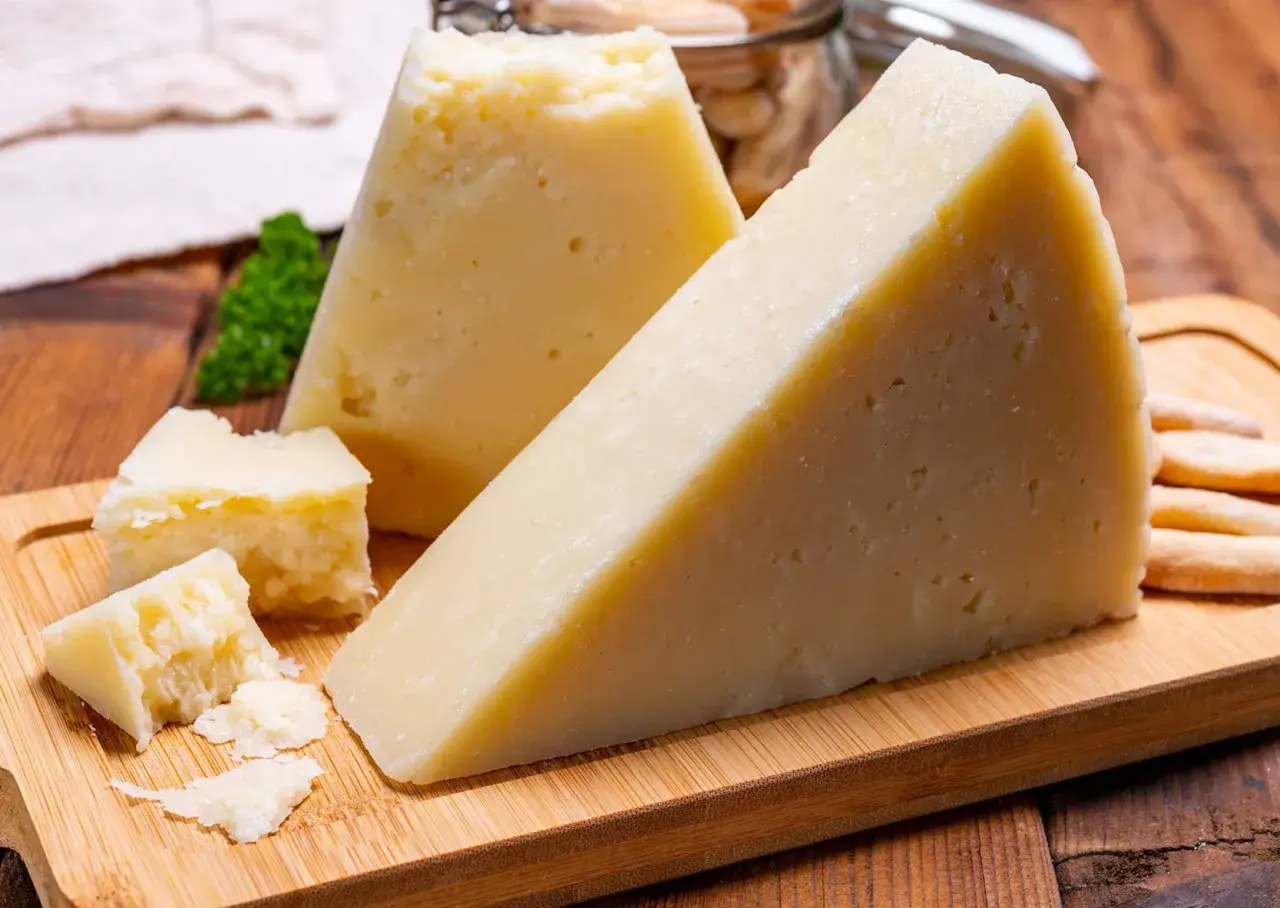 Fette di pecorino stagionato su tagliere di legno, con briciole e grissini sullo sfondo.