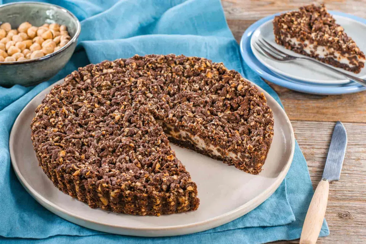 Sbriciolata ricotta e cioccolato con croccante copertura di nocciole e cacao. Una fetta è già servita su un piattino.