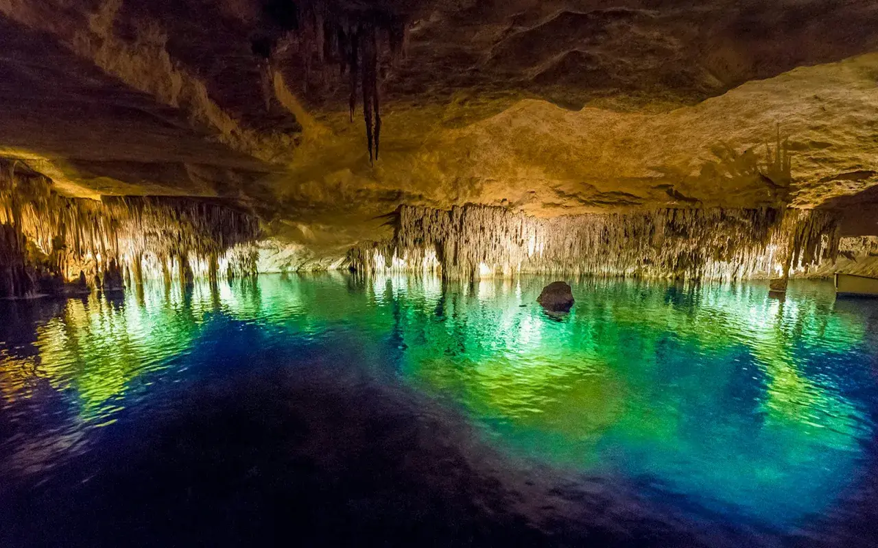 Magiska grottor på Mallorca med turkost vatten som reflekterar stalaktiter och stalagmiter. En båt anas i bakgrunden.