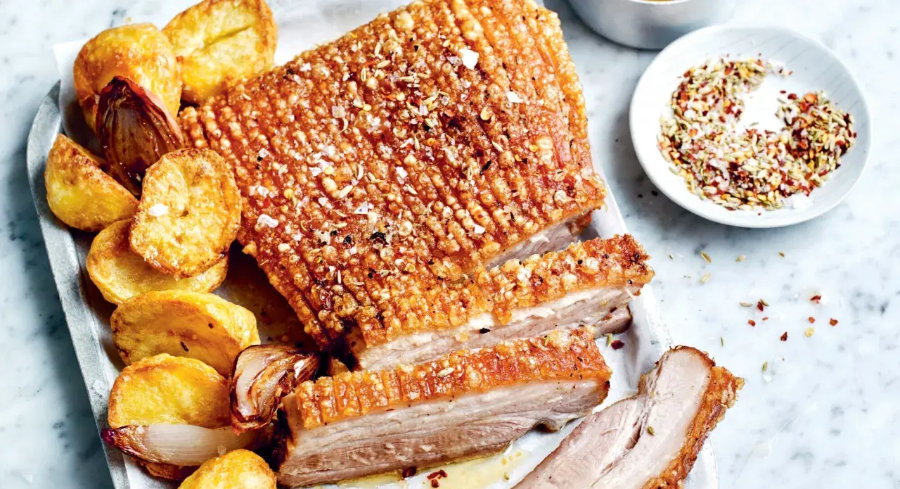 Poitrine de porc croustillante, servie avec des pommes de terre rôties et des oignons caramélisés. Un délice pour les papilles !