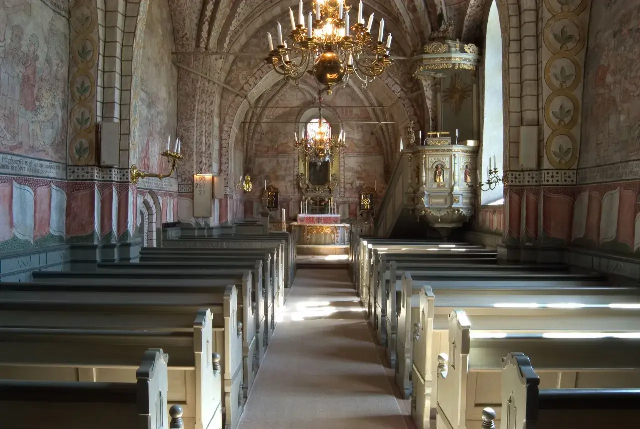Interiör av en kyrka med bänkar, altare och en predikstol. Väggmålningar och en stor ljuskrona skapar en historisk atmosfär. En av många vackra kyrkor i Stockholm.