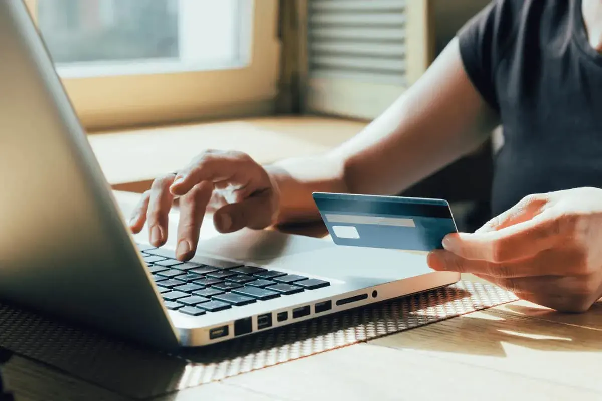Person tippt auf Laptop, hält Visa-Karte. Prüft auf unberechtigte Abbuchung.