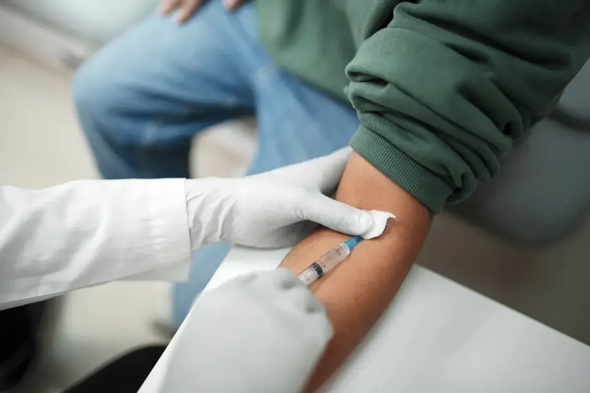 Pobieranie krwi do badań, które mogą pomóc w diagnostyce trzustki. Lekarz w rękawiczkach pobiera krew strzykawką.