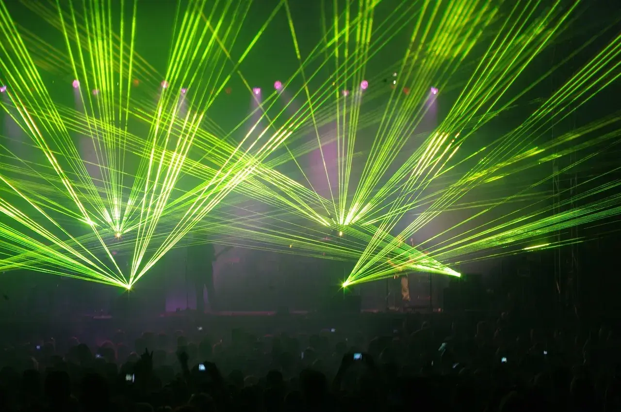 Koncertowe szaleństwo! Zielone lasery rozświetlają scenę, tworząc niesamowitą atmosferę dla zagranicznych legendarnych zespołów rockowych. Tłum szaleje.