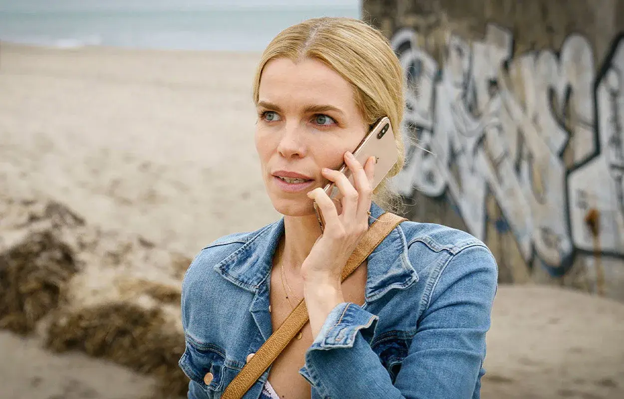 En kvinna i jeansjacka pratar i telefon vid en strand. Kanske en scen från en ny dansk serie på TV4.
