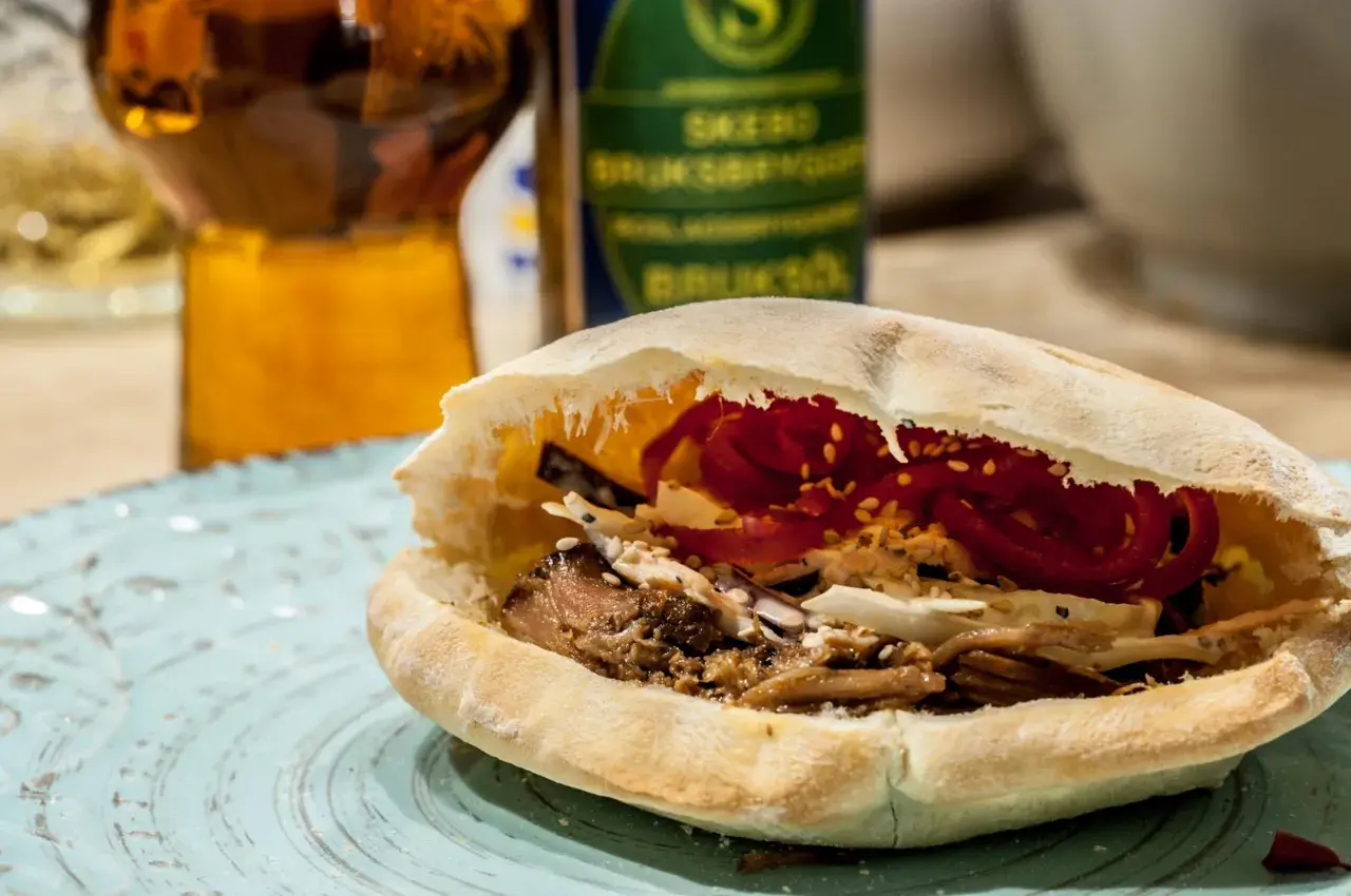 En saftig pulled pork karre-macka i pitabröd, fylld med krispig kål och rödlök. En öl i bakgrunden.