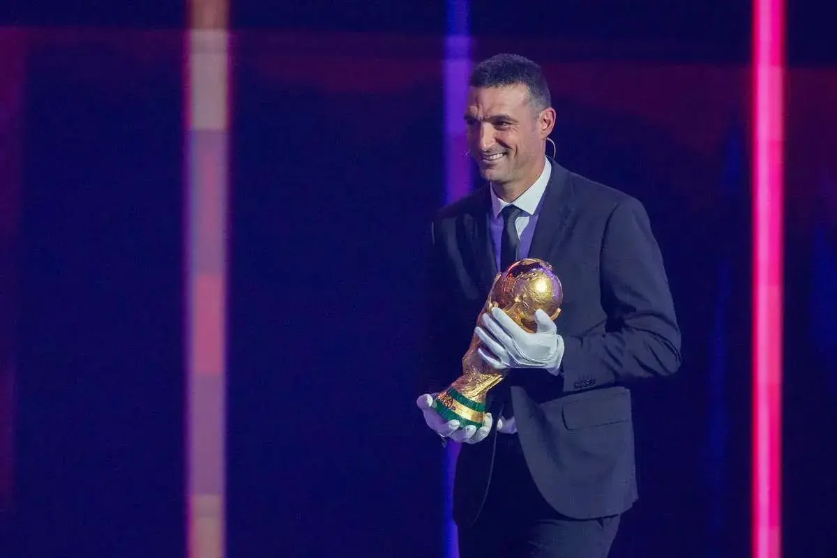 Uśmiechnięty trener Argentyny, Lionel Scaloni, trzyma Puchar Świata w złotych rękawiczkach.