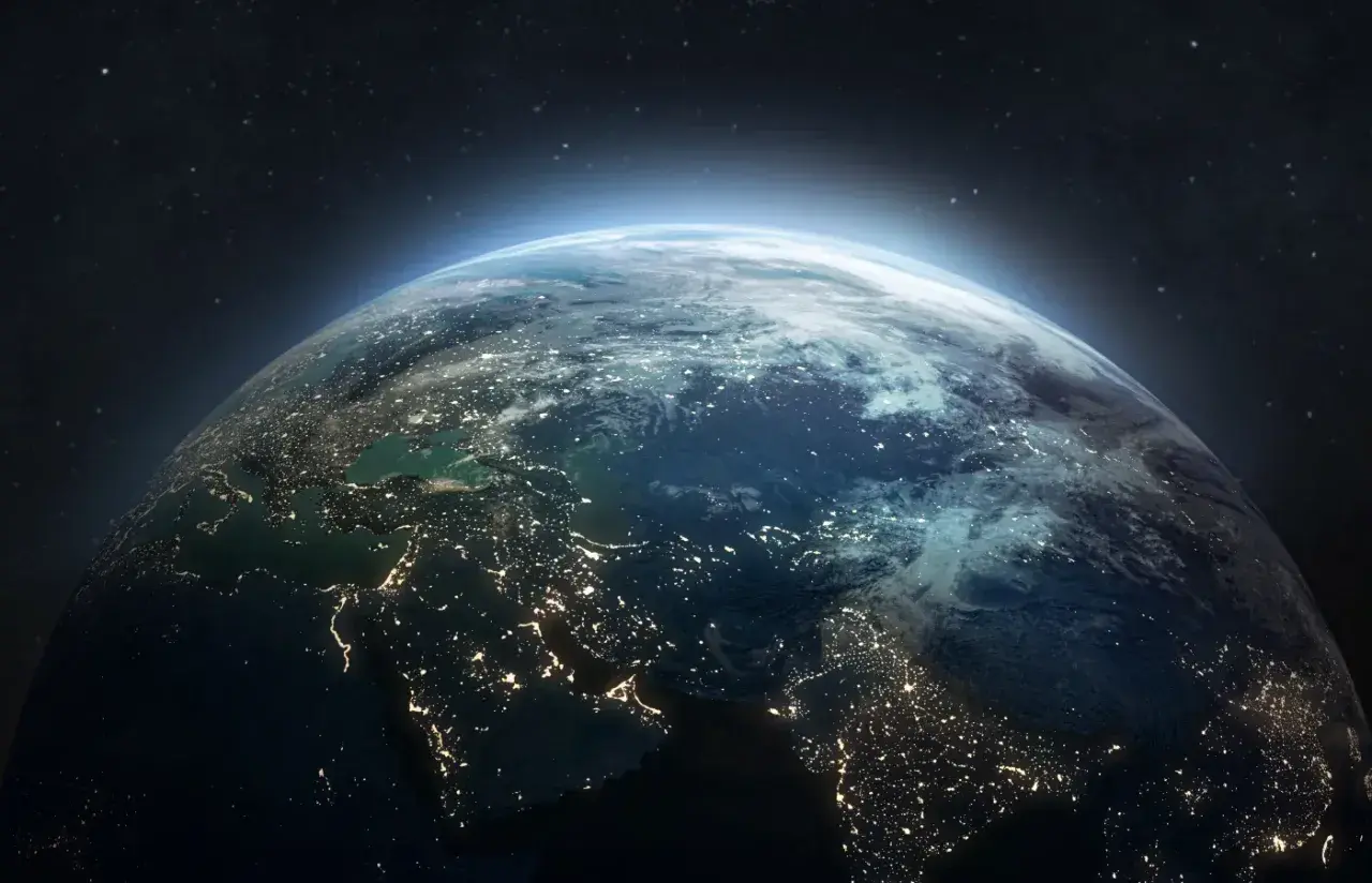 Widok Ziemi z kosmosu nocą, rozświetlonej miastami. W tle gwiazdy i delikatna poświata atmosfery, jakby patrzyły na nią satelity.