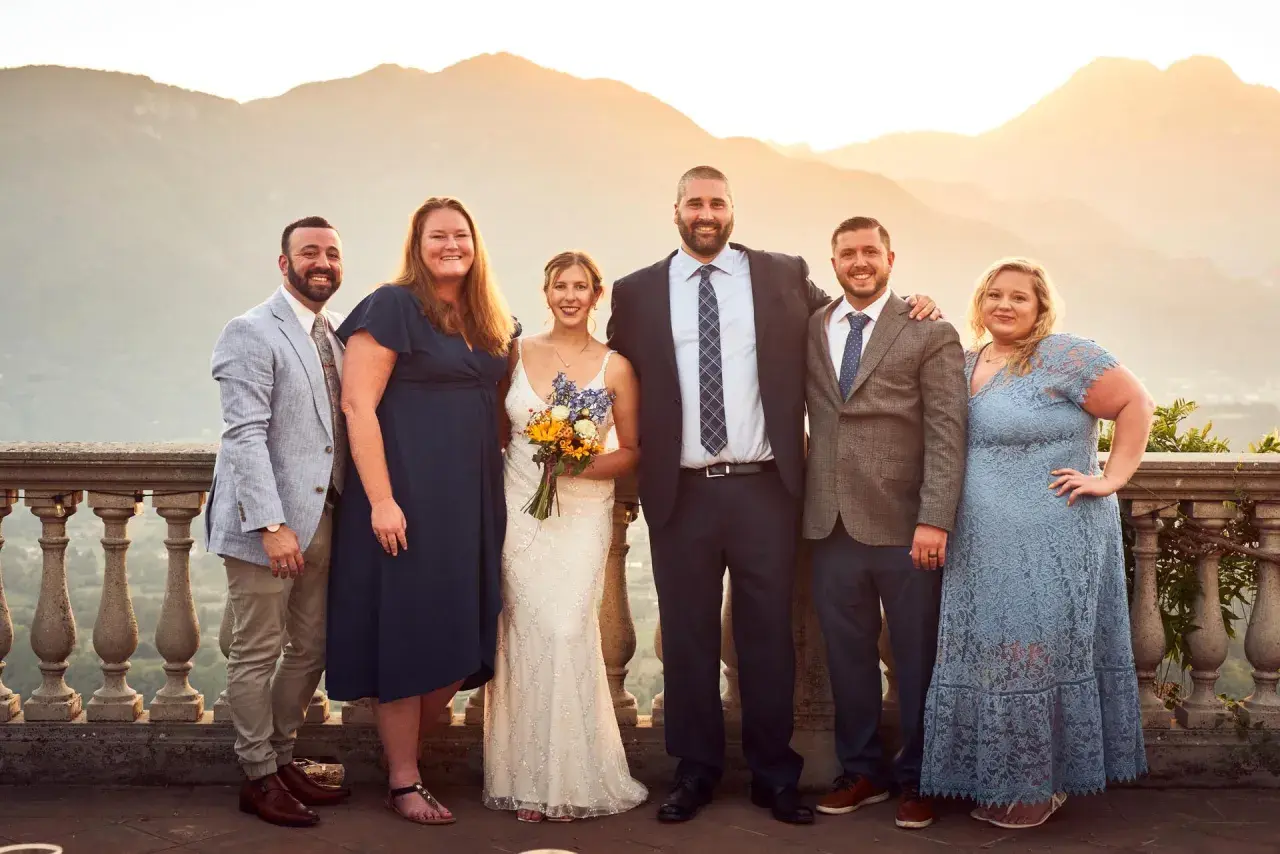 Foto invitati matrimonio: sposi con amici e familiari, con sfondo di montagne al tramonto.