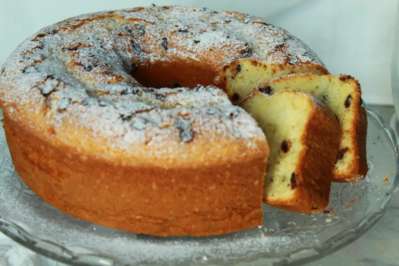Un soffice ciambellone allo yogurt, cosparso di zucchero a velo e gocce di cioccolato, pronto per essere gustato.