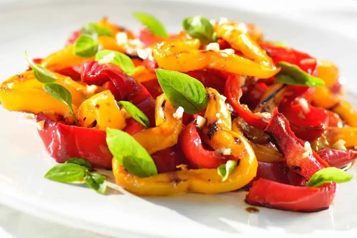 Peperoni al forno colorati, dolci e succosi, guarniti con basilico fresco e aglio. Un contorno estivo perfetto.
