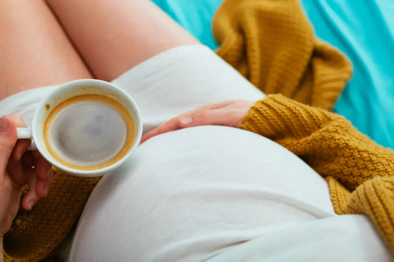 Una donna incinta si gode un caffè, con la mano che accarezza il pancione. Un momento di relax e dolce attesa.
