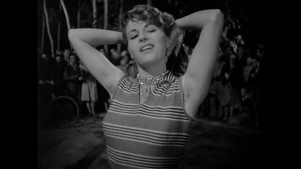 Una donna con le braccia alzate, un sorriso sulle labbra e un'espressione che evoca il "riso amaro significato". Sullo sfondo, una folla indistinta.