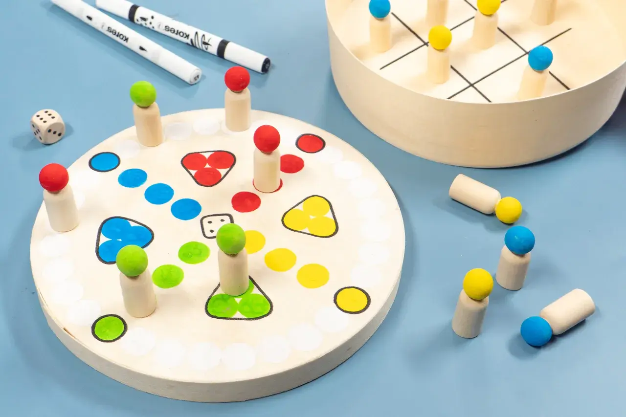 Holzfiguren und Würfel für selbst gebastelte Spiele. Ein Spielbrett mit bunten Feldern und ein Tic-Tac-Toe-Spiel laden zum Spielen ein.