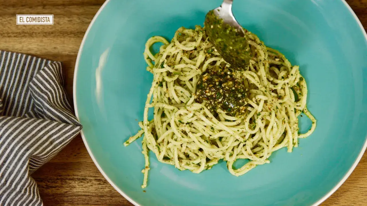 Un plato de pasta al pesto, con una cuchara añadiendo más salsa verde.