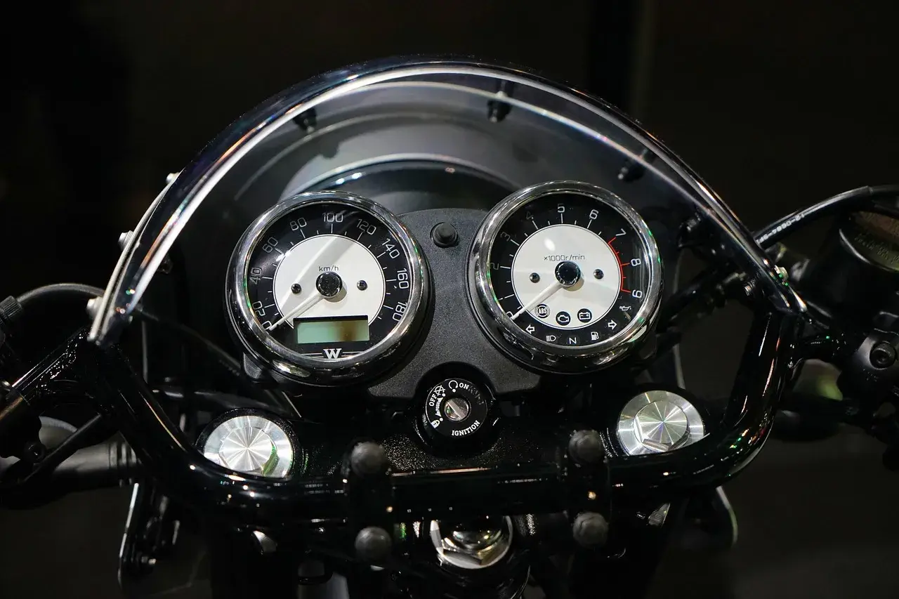 Klasyczny przebieg motocykla: prędkościomierz i obrotomierz w chromowanych obudowach, podświetlane kontrolki i kluczyk zapłonu.