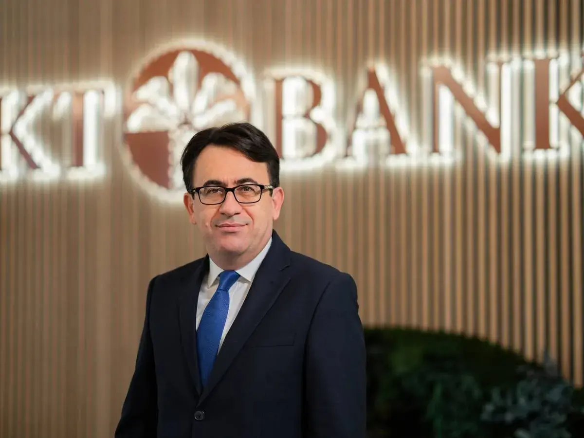 Mann in Anzug vor KT Bank Logo. Positive KT Bank Erfahrung durch professionelles Auftreten.