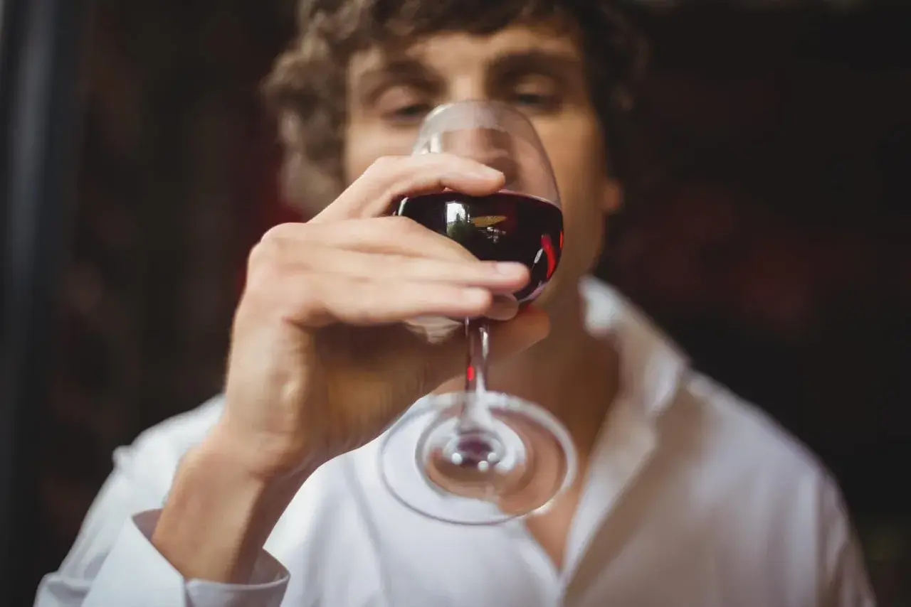 Un homme déguste un verre de vin rouge, savourant le langage du vin.