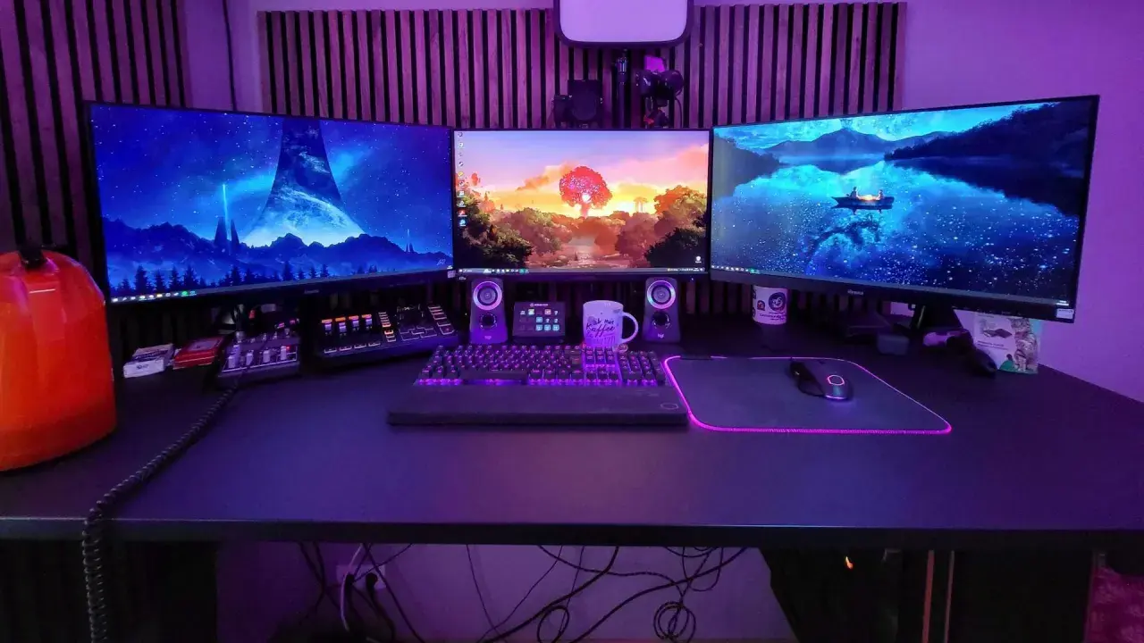 Ein episches **gaming set up** mit drei Monitoren, beleuchteter Tastatur und Maus. Im Hintergrund leuchtet lila Beleuchtung.