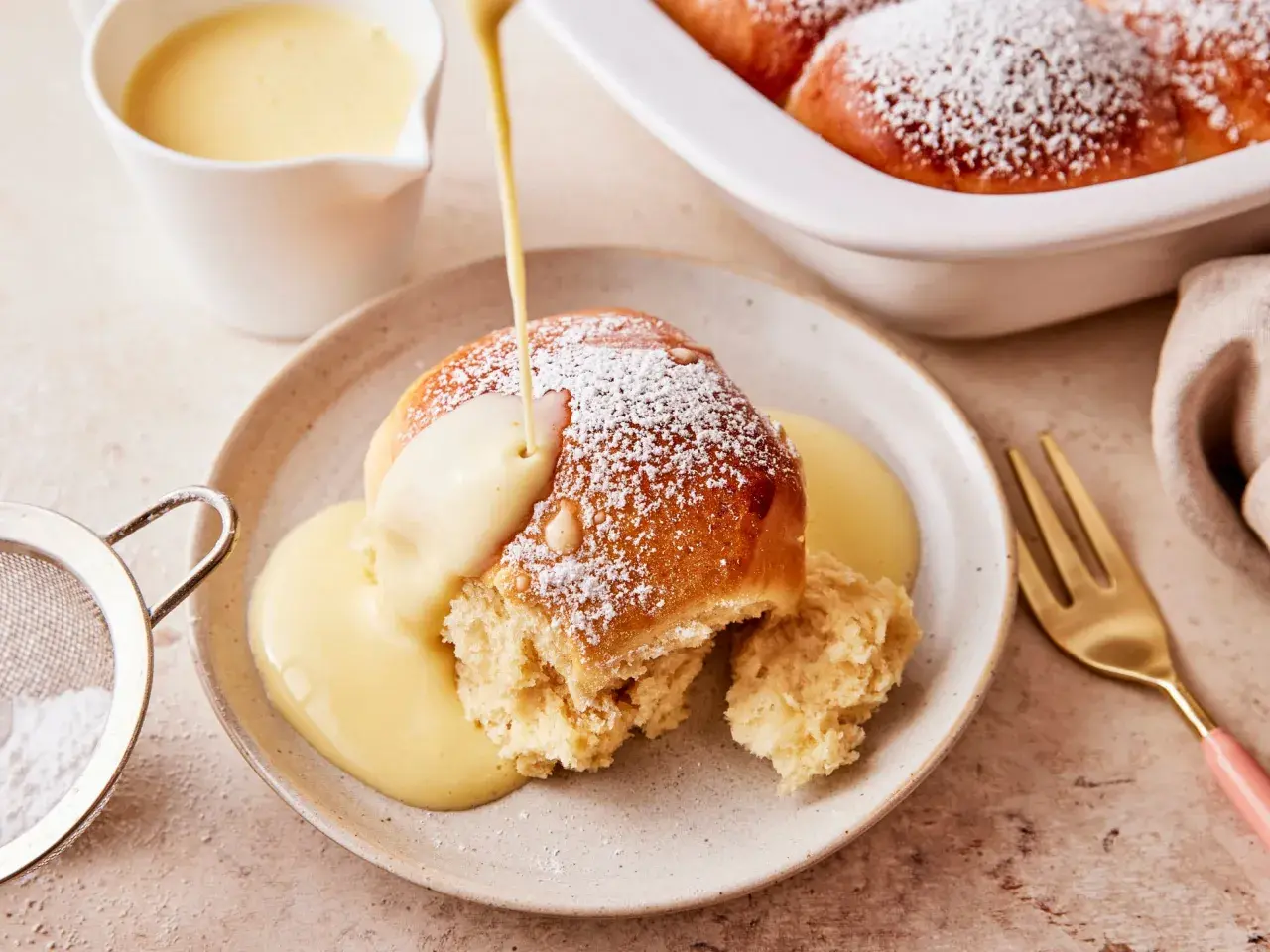 Ein Buchtel wird mit Vanillesauce übergossen, bestäubt mit Puderzucker. Ein köstliches Buchteln Rezept zum Genießen.