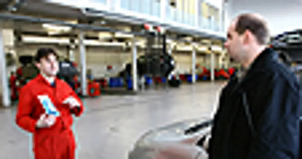 Mechanik w czerwonym kombinezonie omawia z klientem kwestie związane z ekologicznym paliwem, takim jak biodiesel, w warsztacie samochodowym.