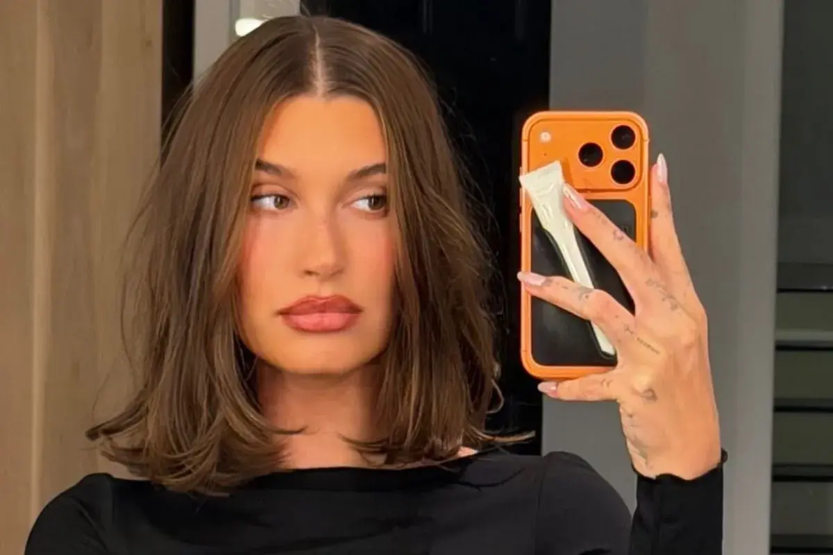 En kvinna med fina hårfrisyrer tar en selfie med sin orangea mobil.