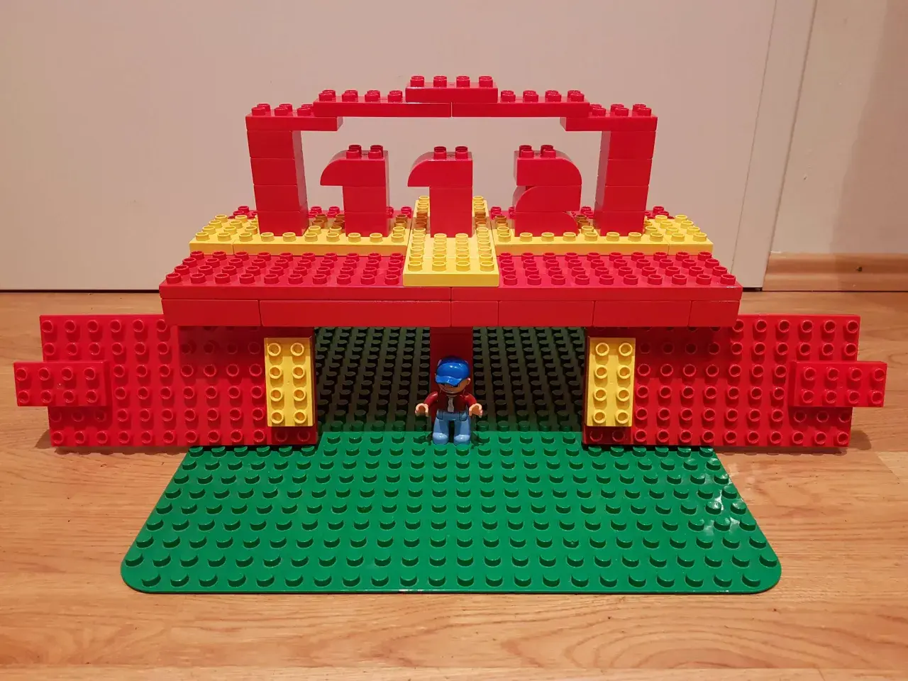 Ein kleiner Junge steht unter einem roten und gelben LEGO Duplo Tor, das wie eine Feuerwache aussieht. Die Zahl 112 ist darauf abgebildet.