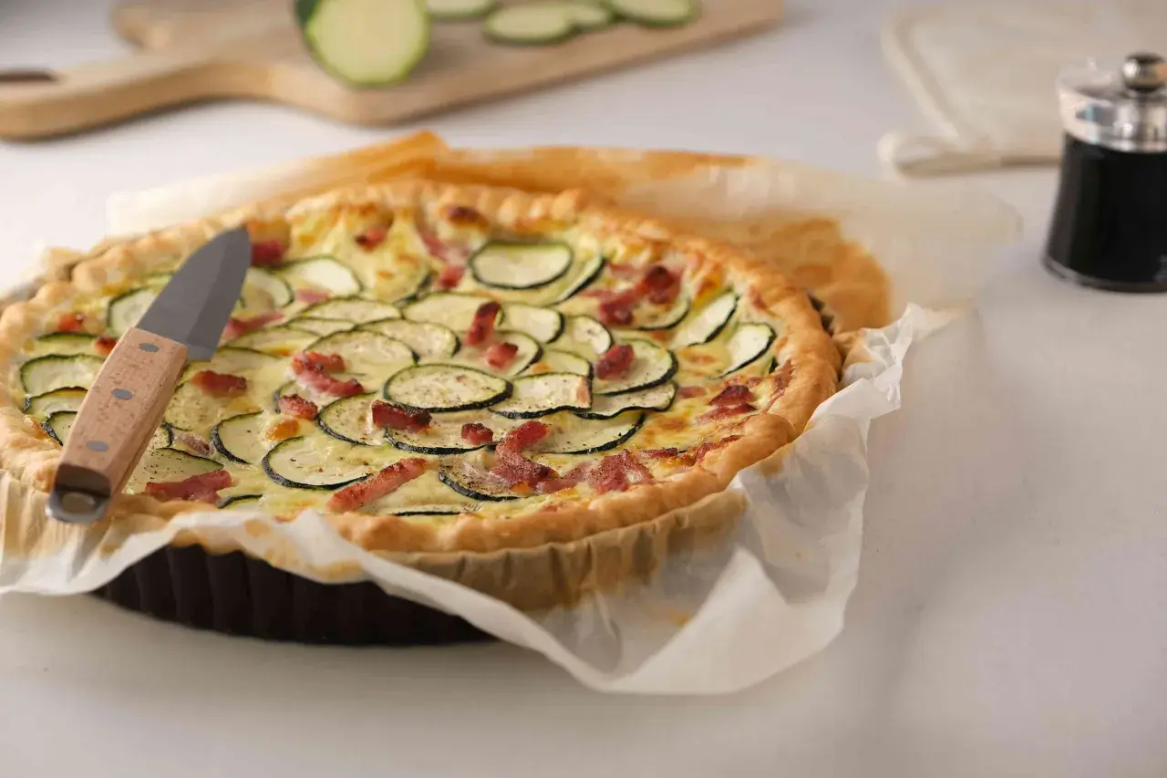 Une délicieuse quiche courgette lardon dorée, garnie de rondelles de courgettes et de lardons croustillants, prête à être dégustée.