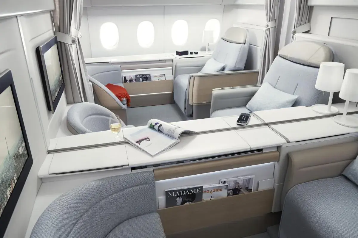 Luxuriöse Sitze in der **first class** eines Flugzeugs, mit Magazinen, einem Glas Wein und Bildschirmen.