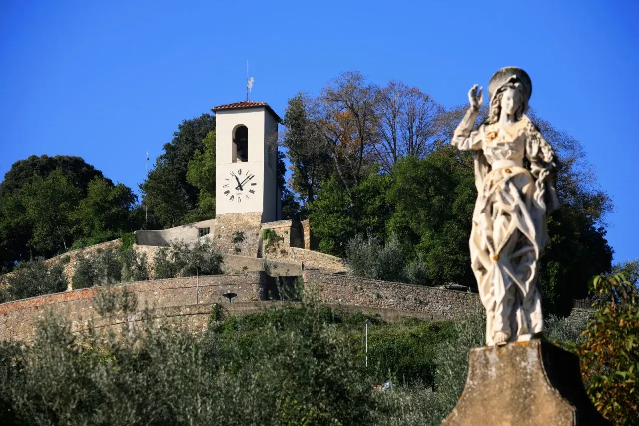 Statua di santo e torre dell'orologio su una collina verdeggiante, un'immagine che cattura l'essenza di cosa vedere ad Artimino.