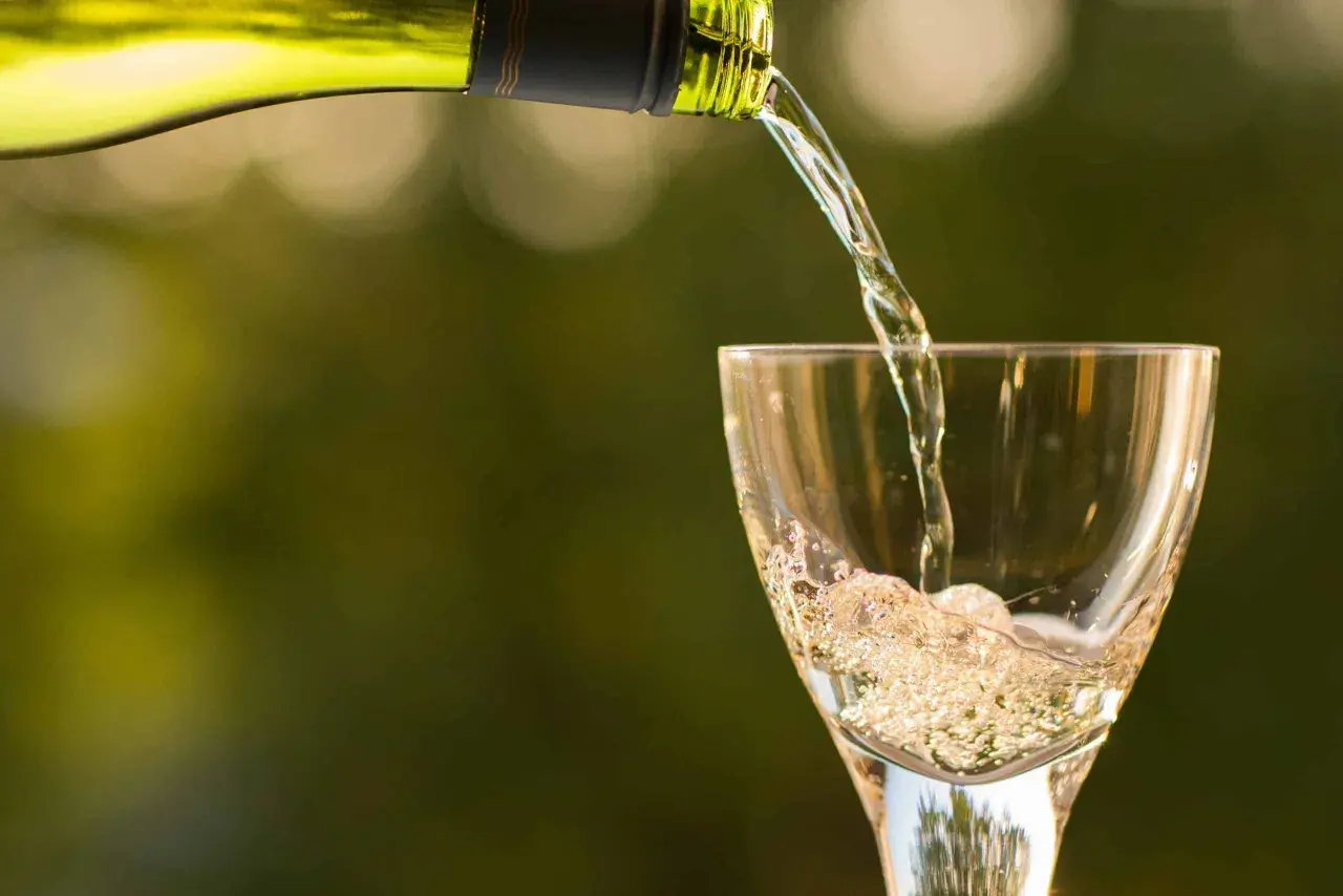 Un vin blanc pétillant est versé dans un verre, créant une mousse légère qui rappelle le sucre dans le vin.