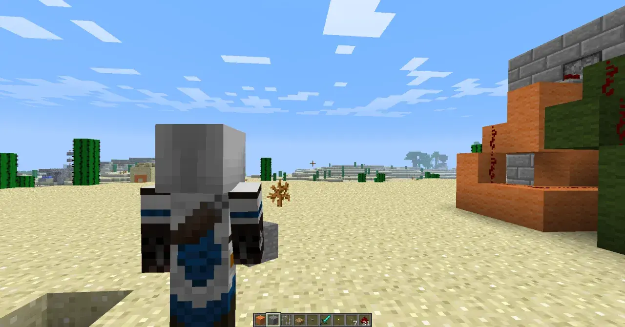 Postać w grze Minecraft stoi na pustyni, obok niej widać mechanizm z pomarańczowych bloków i czerwonego proszku.