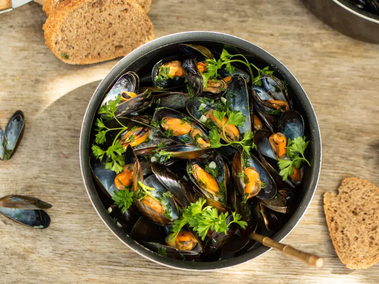 Un plat généreux de moules marinières, garni de persil frais, servi avec du pain de campagne sur une table en bois.