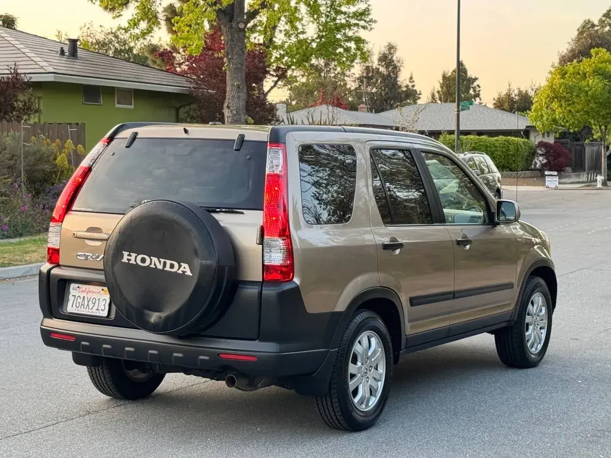 En gyllene Honda CRV 2005 står parkerad på en gata, med reservhjulet synligt på bakluckan.