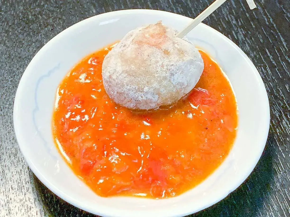En boll med potatis doppad i en kryddig mojo rojo-sås.