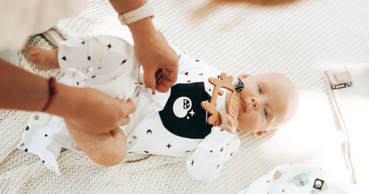 22 stopnie w domu? Niemowlaka ubieramy lekko. Na zdjęciu maluch w body z gwiazdkami i księżycami, z gryzakiem w kształcie renifera.