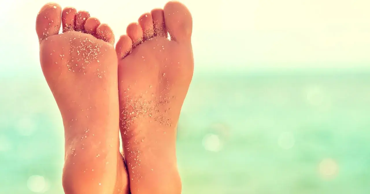 Stopy z piaskiem na plaży, z widocznym płaskostopiem.