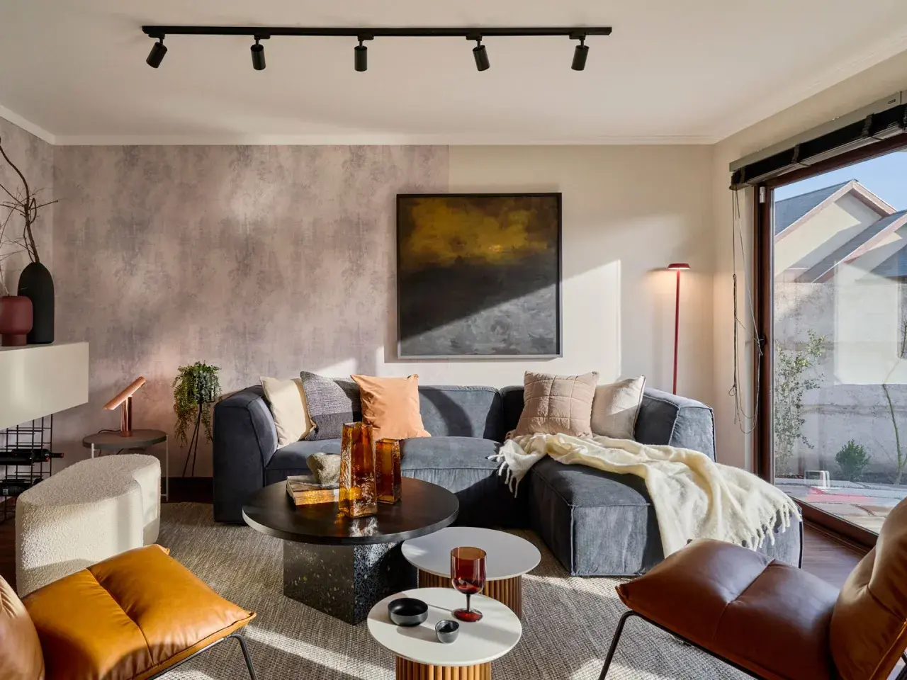 Sofá gris, mesas de centro, sillones de cuero y detalles decorativos. Los **colores que dan luz y amplitud** crean un ambiente acogedor y moderno.