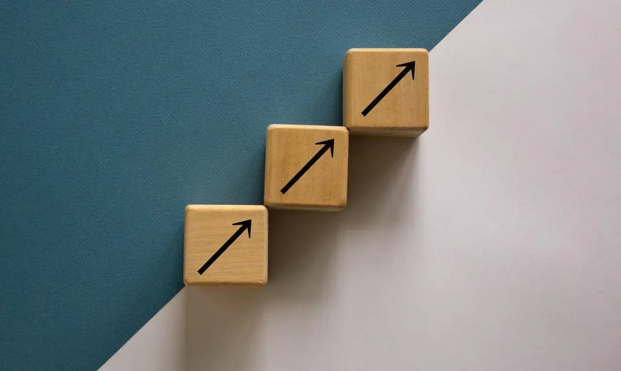 Trzy drewniane kostki tworzą schody, każda z czarną strzałką w górę. To symboliczne ten square games akcje, które rosną.