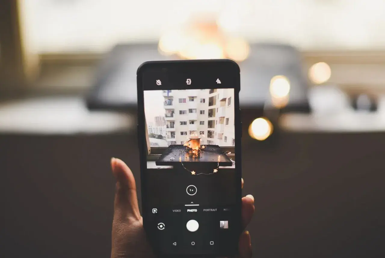 Smartfon robi zdjęcie kubka z napojem i światełek. To przykład fotografii produktowej.