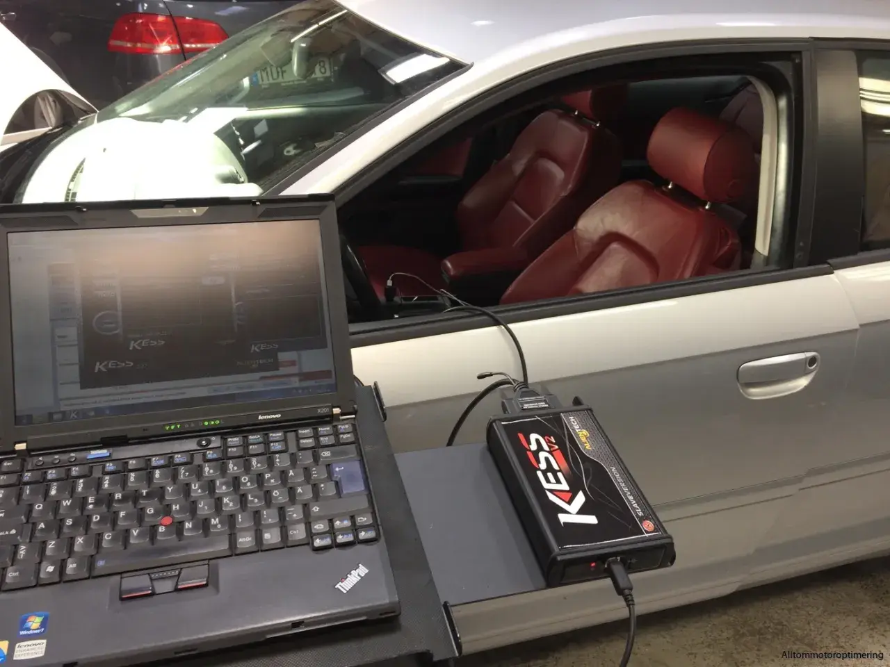 Laptop och KESS-enhet kopplade till en bil för att chippa bilen. Röd läderinredning syns i kupén.