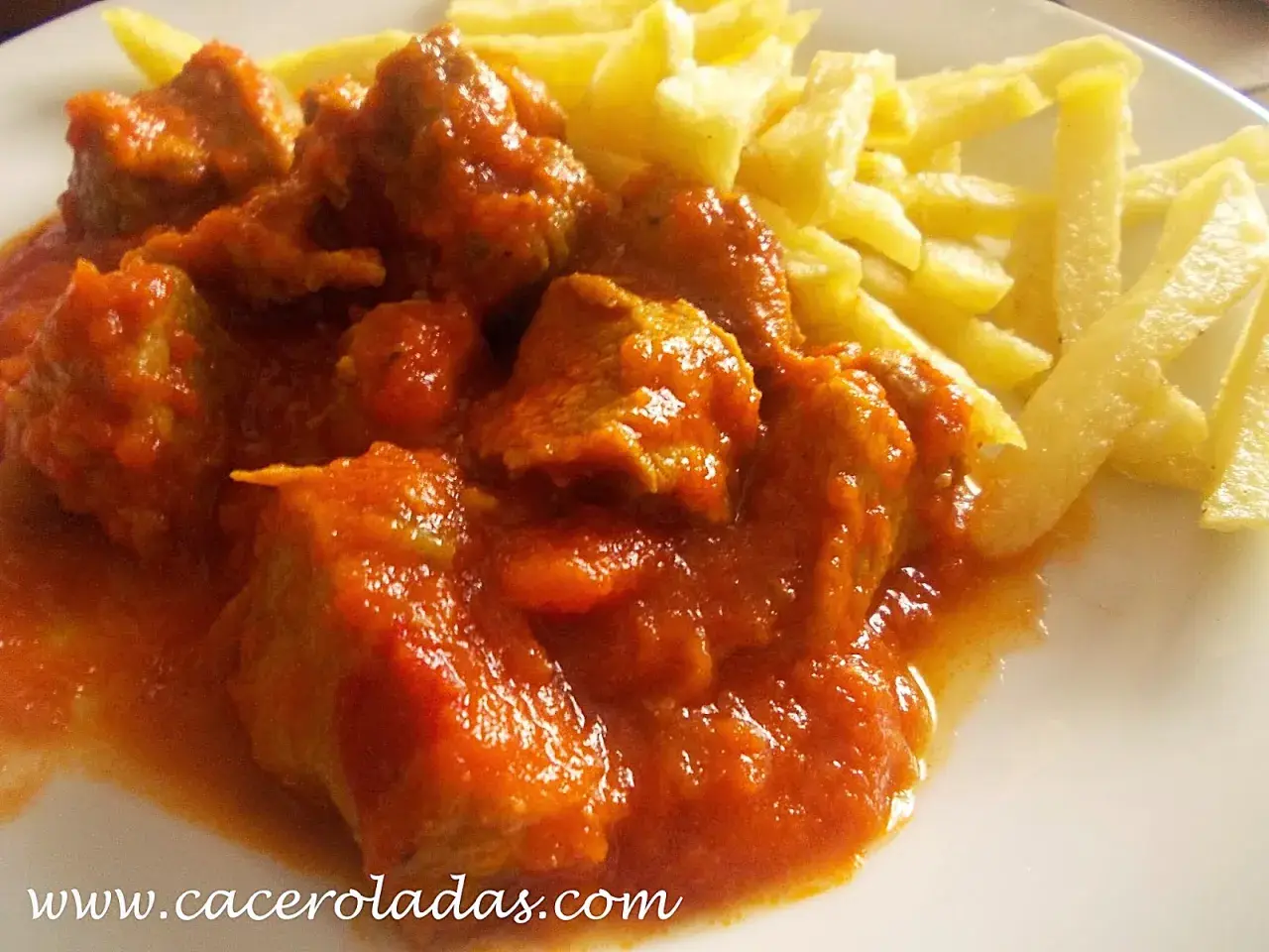 Sabroso carne de cerdo con tomate de la abuela, jugoso y tierno, acompañado de patatas fritas crujientes.