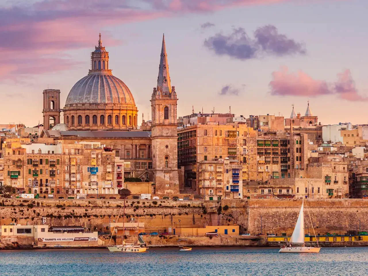 Sonnenuntergang über Valletta, Malta. Die Kuppel der St. Paul's Cathedral und Segelboote spiegeln sich im Wasser. Tolle Urlaub in Malta Erfahrungen!