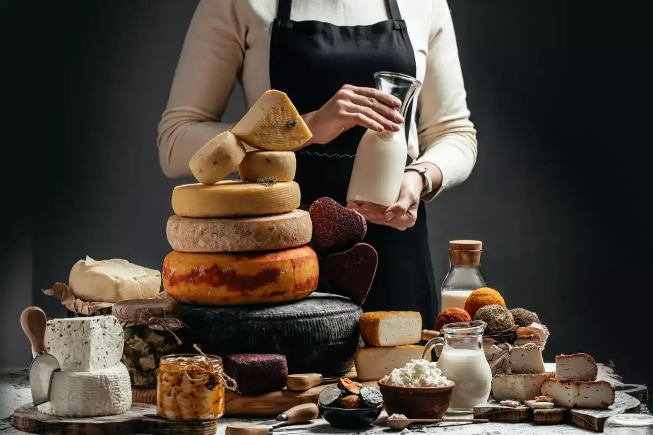 Una ricca selezione di formaggio a latte crudo, tra cui forme rotonde e quadrate, con latte fresco in caraffa.
