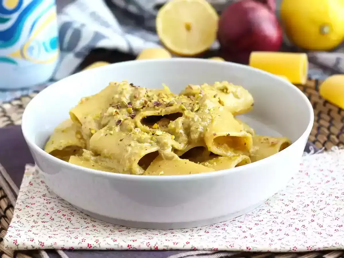 Piatto di pasta tonno e limone, condita con una crema verde e pistacchi tritati, servita in una ciotola bianca.