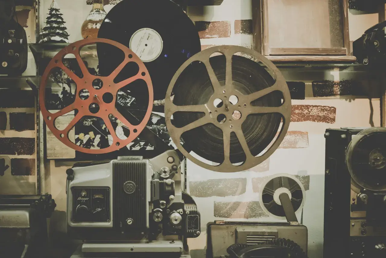 Stary projektor filmowy, taśmy filmowe i płyta winylowa na tle ceglanej ściany.