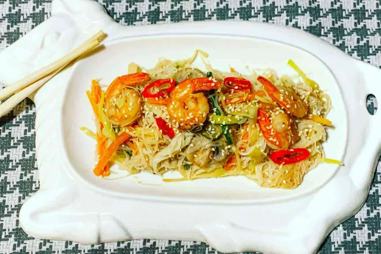 Deliziosi spaghetti di riso con gamberi succulenti e verdure croccanti, guarniti con semi di sesamo.