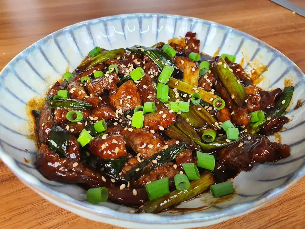 Un plat appétissant de boeuf aux oignons, garni de graines de sésame et d'oignons verts frais.
