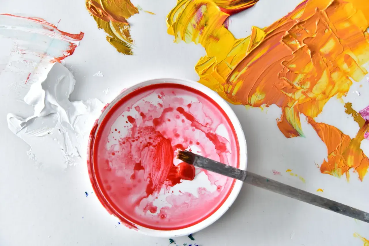 Pennello intinge nel rosso per capire come miscelare i colori per pittura murale. Macchie di giallo e arancio vibrante completano la scena.