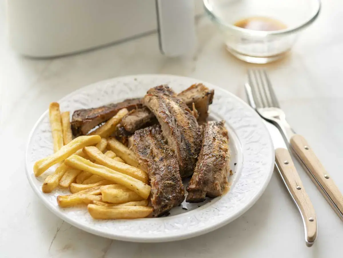 Costillas jugosas y patatas fritas crujientes, recién salidas de la freidora de aire. Un plato perfecto para disfrutar.